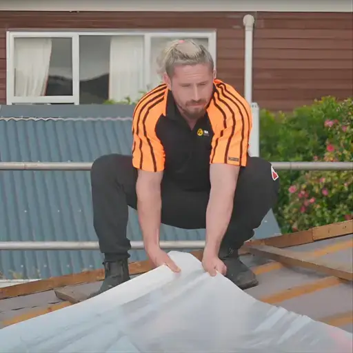 Ryan Franklin of AMR TEAM on a roof laying shrink-wrap for asbestos removal preparation